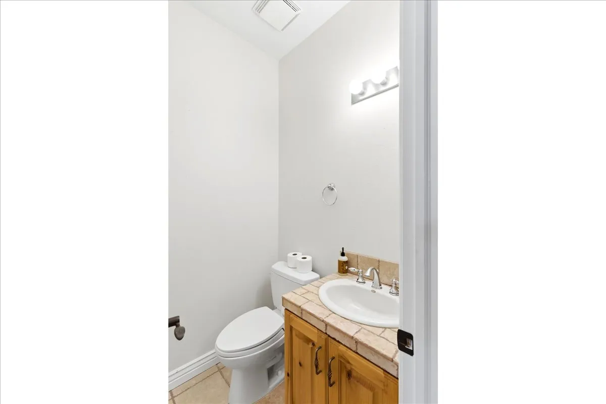 Compact bathroom featuring a white toilet, a vanity with wood cabinetry, a tile countertop, and a white drop-in sink