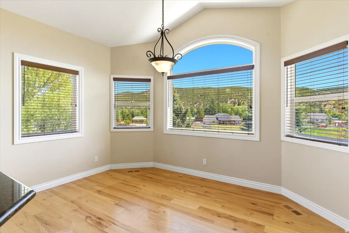 Arched window with mountain scenery, wood-finish flooring, vaulted ceiling, and decorative pendant lighting