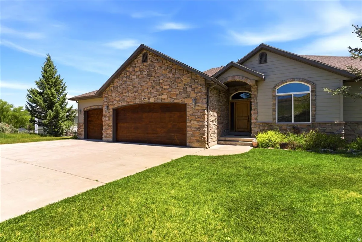 Stone and siding exterior with a prominent arched entry, wood-finish garage doors, and a concrete driveway