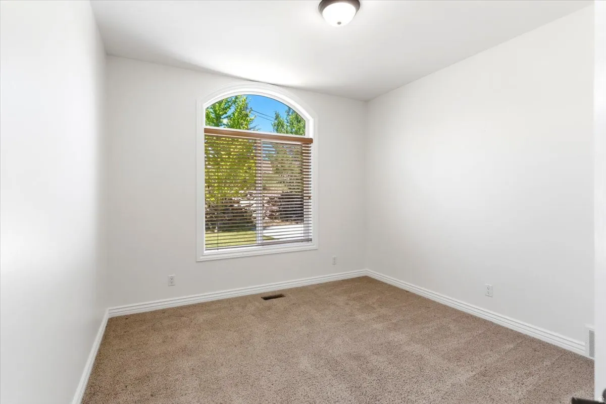 Room featuring an arched window with horizontal blinds, neutral-toned carpet, and white baseboards