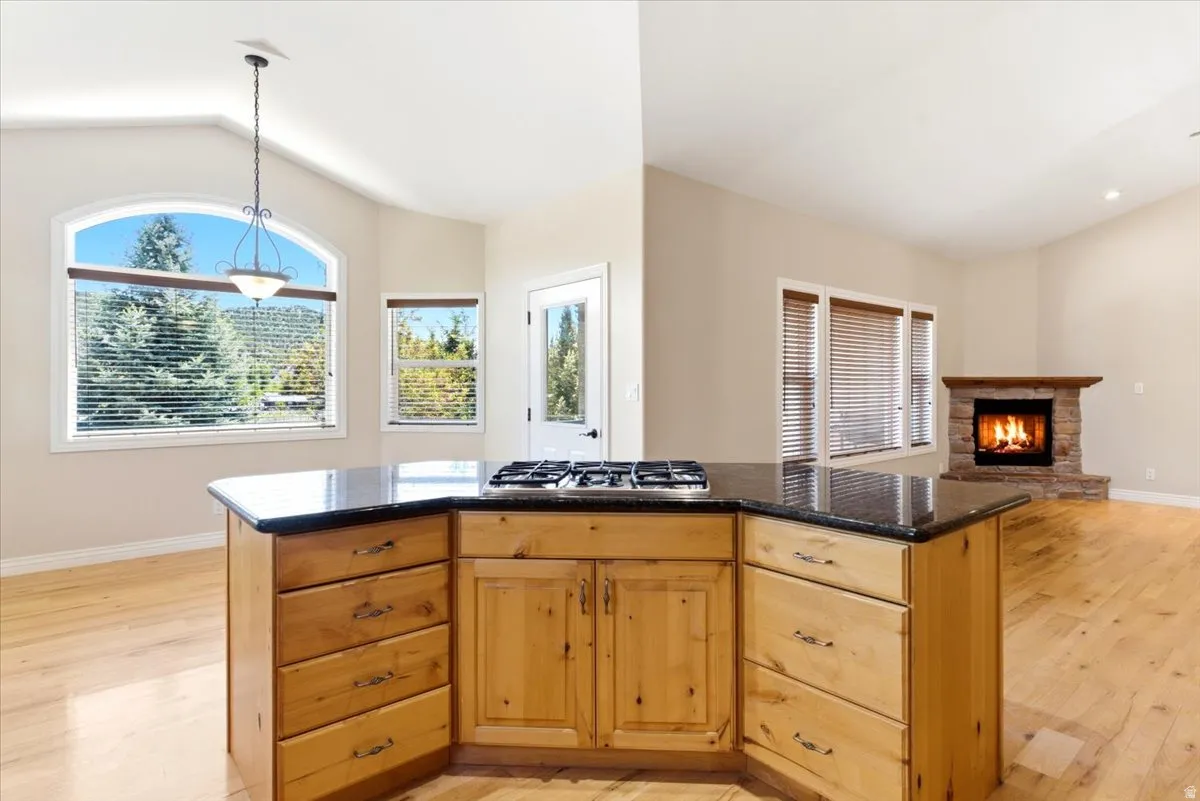 Kitchen island with integrated cooktop, granite countertop, and natural wood cabinetry