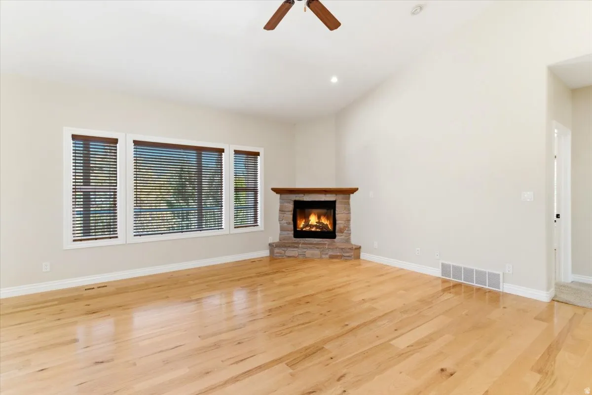 Spacious living area featuring light wood-finish flooring, a stone-clad fireplace with a wood mantel, and a vaulted ceiling