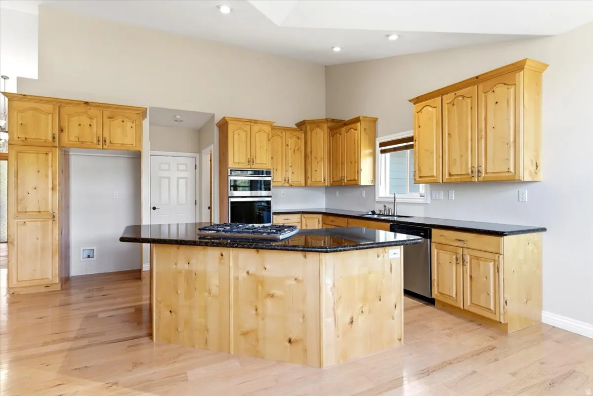 Kitchen featuring light wood cabinetry, dark countertops, a central island with a built-in cooktop, light wood-finish flooring, and recessed lighting