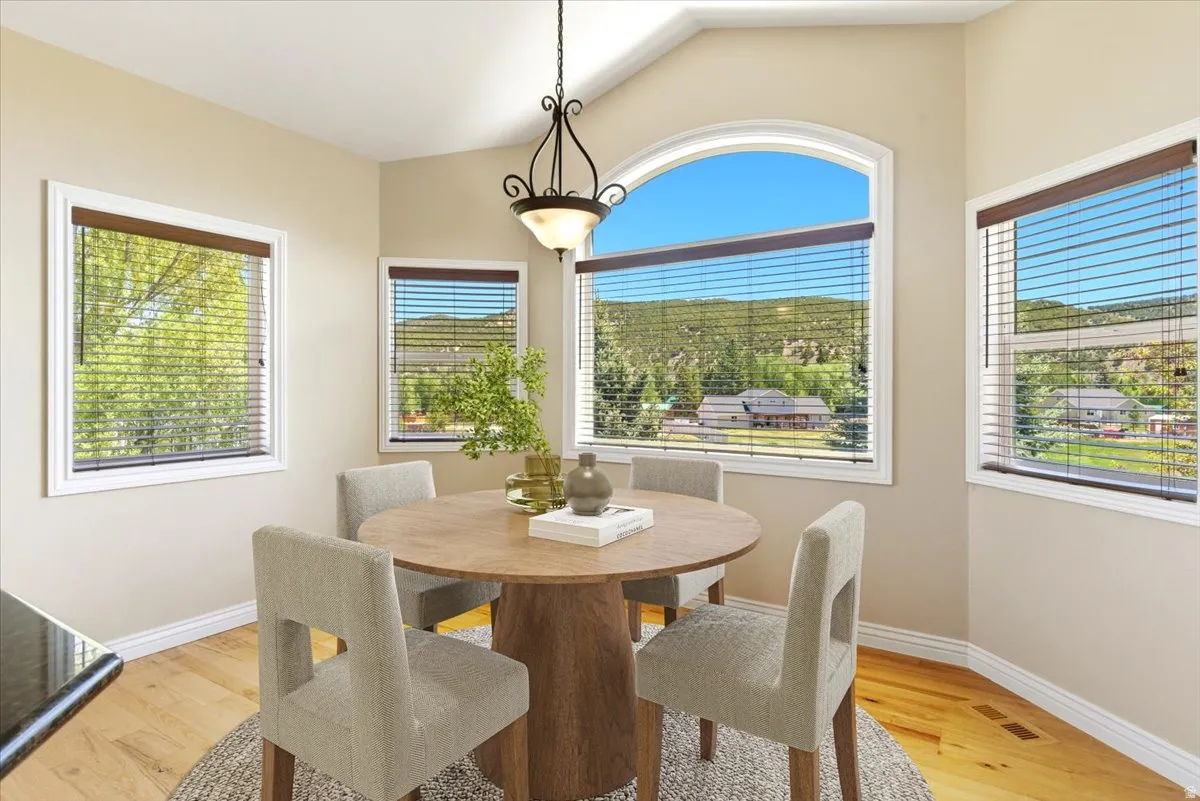 Dining area featuring an arched picture window, additional rectangular windows with blinds, wood-finish flooring, and a decorative pendant light fixture. Virtually staged.
