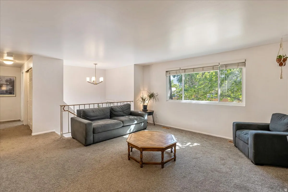 Bright living area featuring a large picture window, neutral carpeting, white walls, and a contemporary chandelier