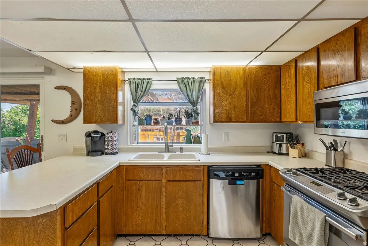U-shaped kitchen featuring wood cabinetry, white countertops, a double-basin sink, and integrated stainless steel appliances including a gas range and dishwasher