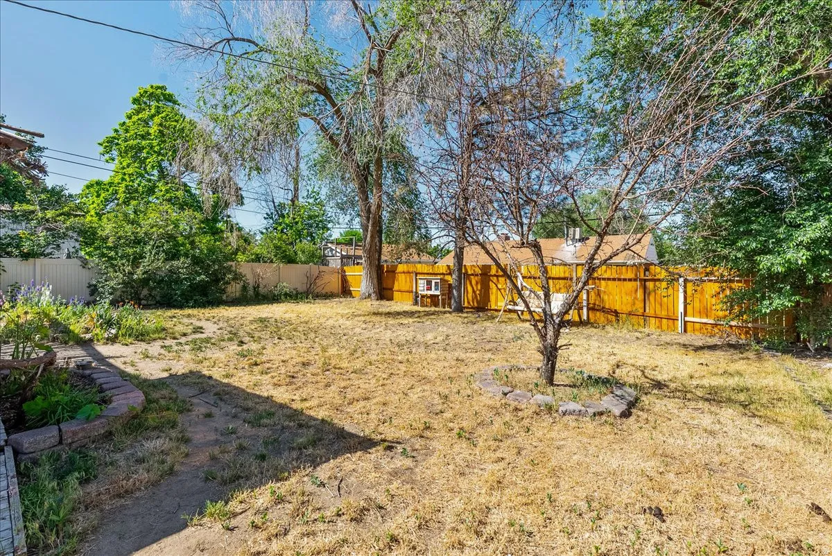 Expansive backyard space featuring mature trees, a stone-bordered planting area, and privacy fencing