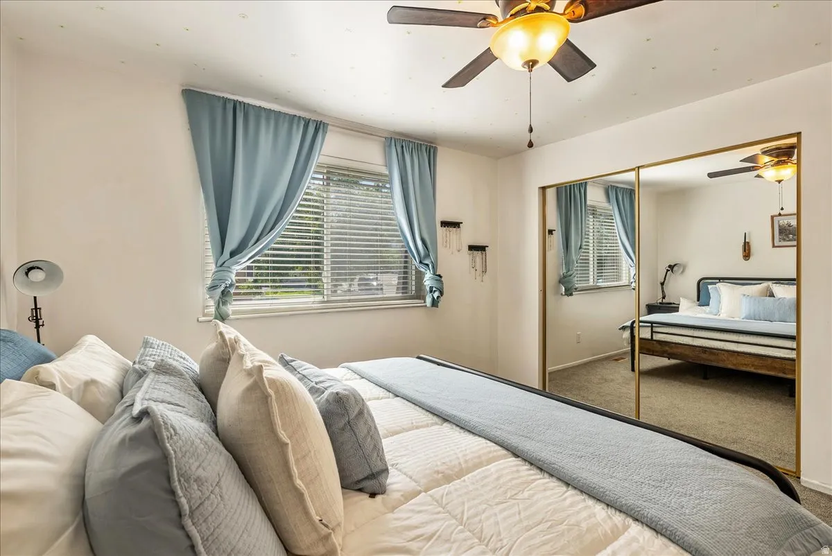 Bedroom featuring a ceiling fan with integrated lighting, a window with horizontal blinds, and full-wall mirrored closet doors with gold-toned framing