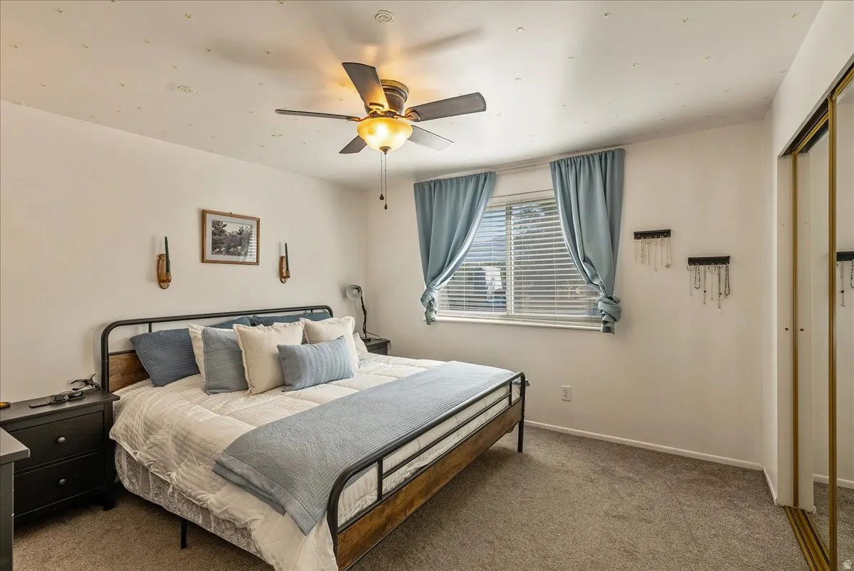 Bedroom featuring a ceiling fan with integrated lighting, a window with blinds and drapes, and a mirrored closet