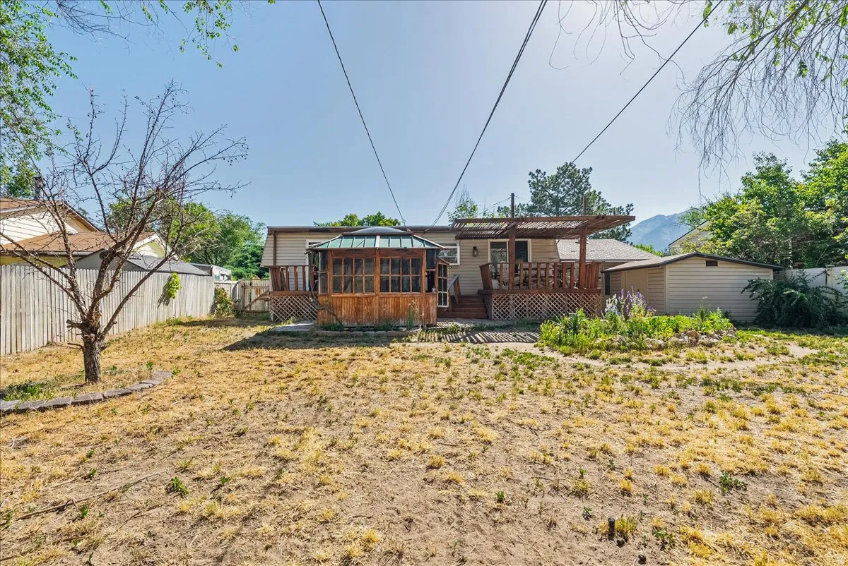 Spacious backyard featuring a wooden deck with a pergola, an enclosed gazebo, and a storage shed