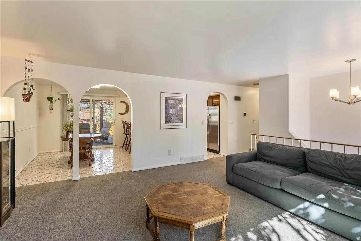 Carpeted living space featuring arched doorways, a railing-lined staircase, and a contemporary chandelier