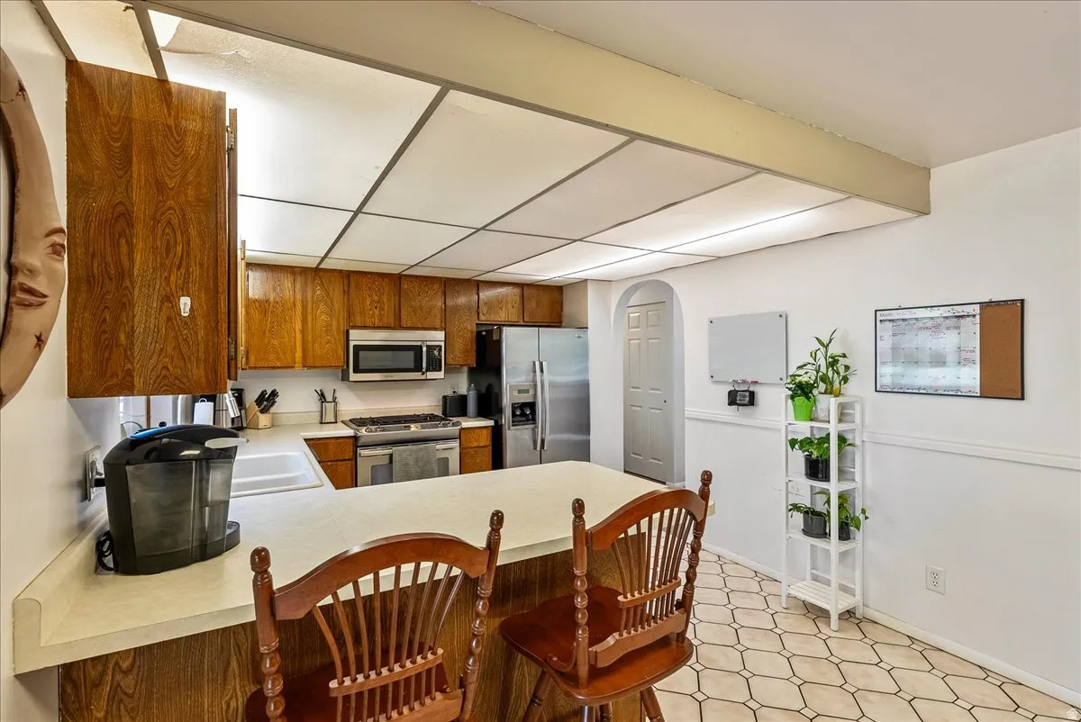 Kitchen featuring wood cabinetry, stainless steel appliances, a white sink, and a light-toned countertop