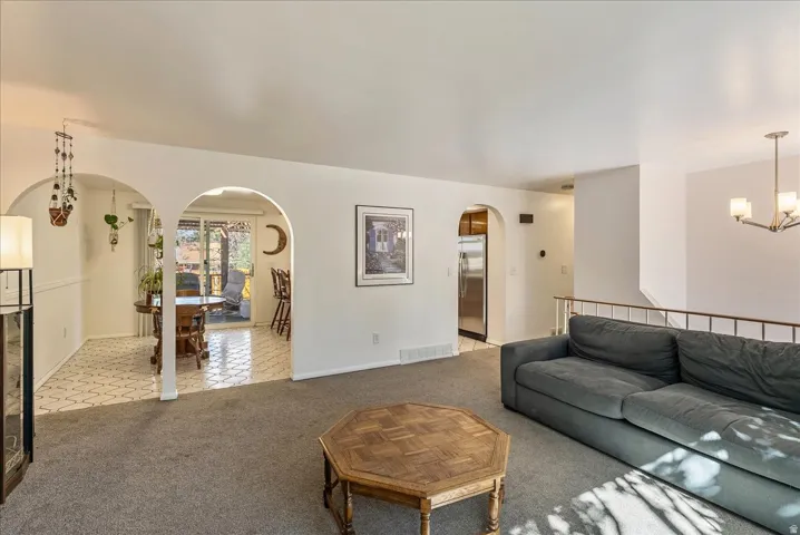 Carpeted living space featuring arched doorways, a railing-lined staircase, and a contemporary chandelier