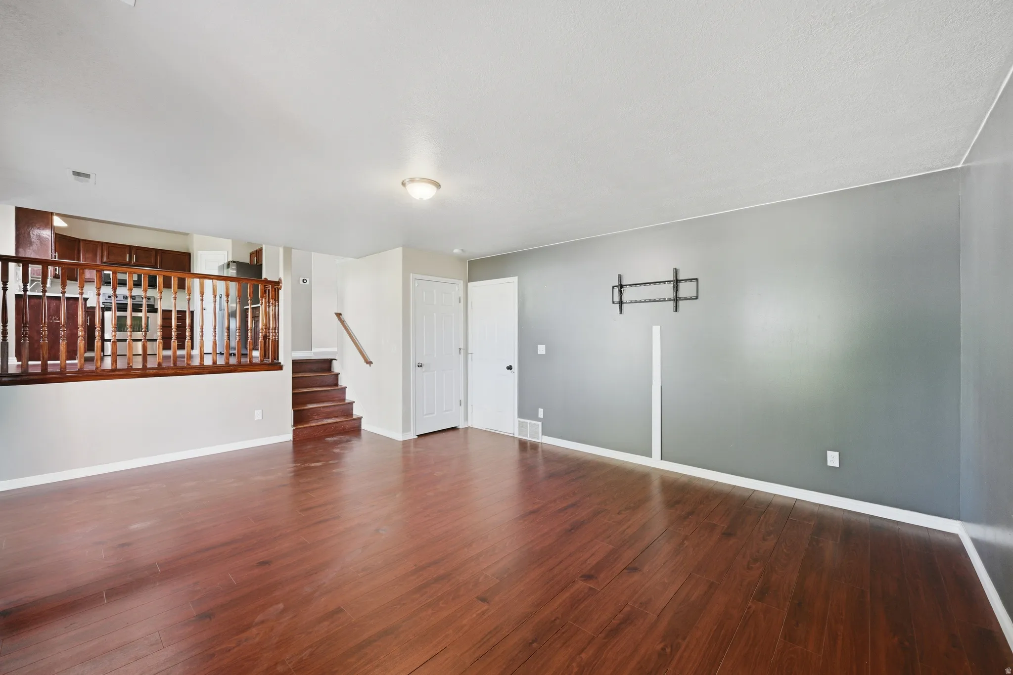 Open-concept living area featuring rich wood-finish flooring, a neutral color palette, and a half-wall with wood balusters