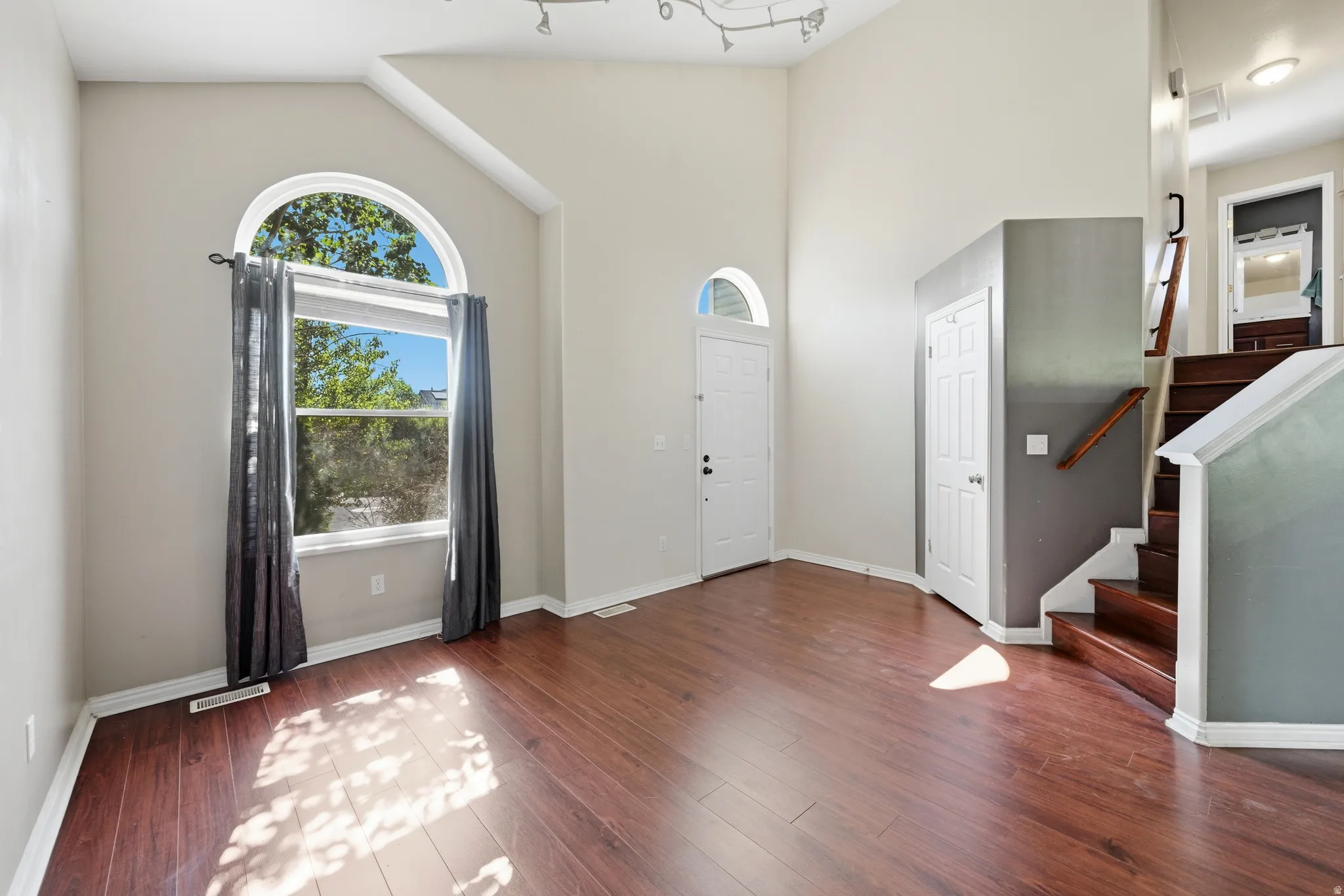 Spacious entry featuring high ceilings, wood-finish flooring, a prominent arched window, a solid entry door with an arched transom, and a staircase with a wood handrail