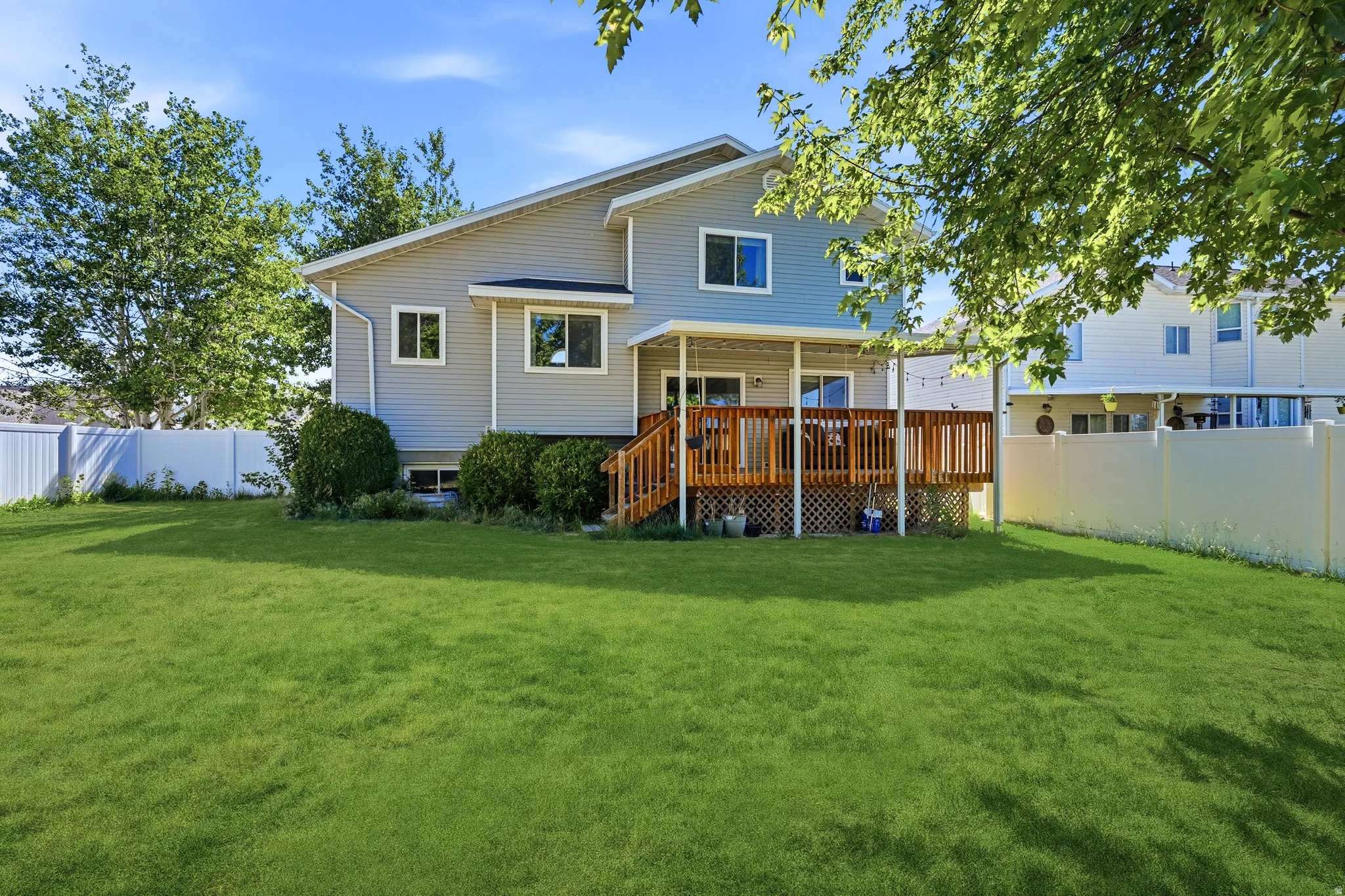 Expansive rear lawn featuring a multi-level wood deck with lattice skirting and a covered patio area
