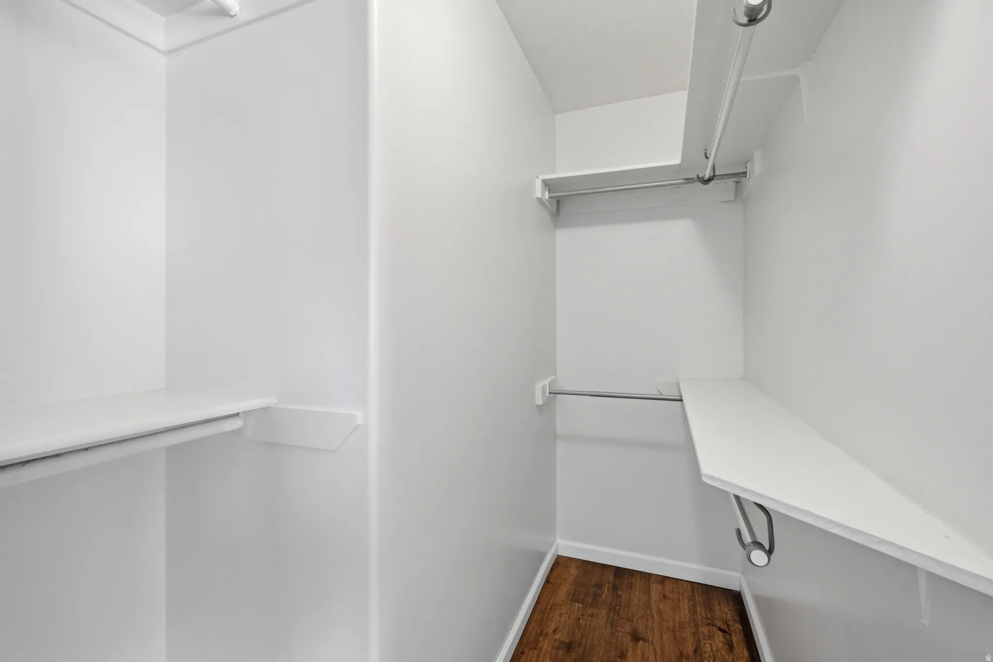 Walk-in closet featuring white walls, durable wood-finish flooring, and multiple levels of shelving and hanging rods for organizational potential