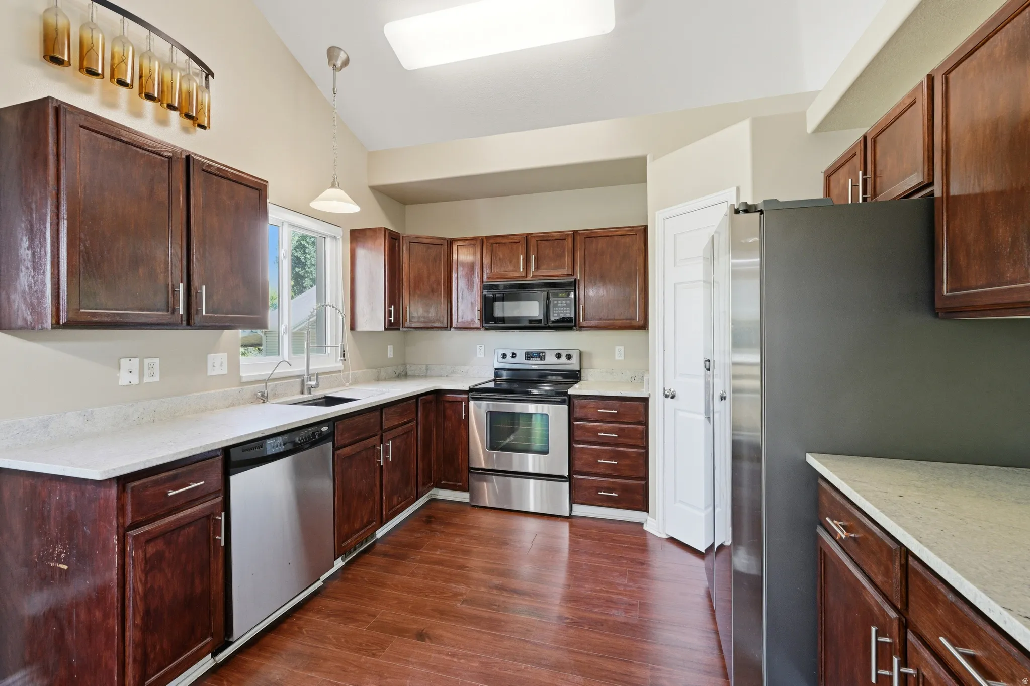 Kitchen featuring wood-finish flooring, dark wood cabinetry, light countertops, stainless steel appliances, and a vaulted ceiling