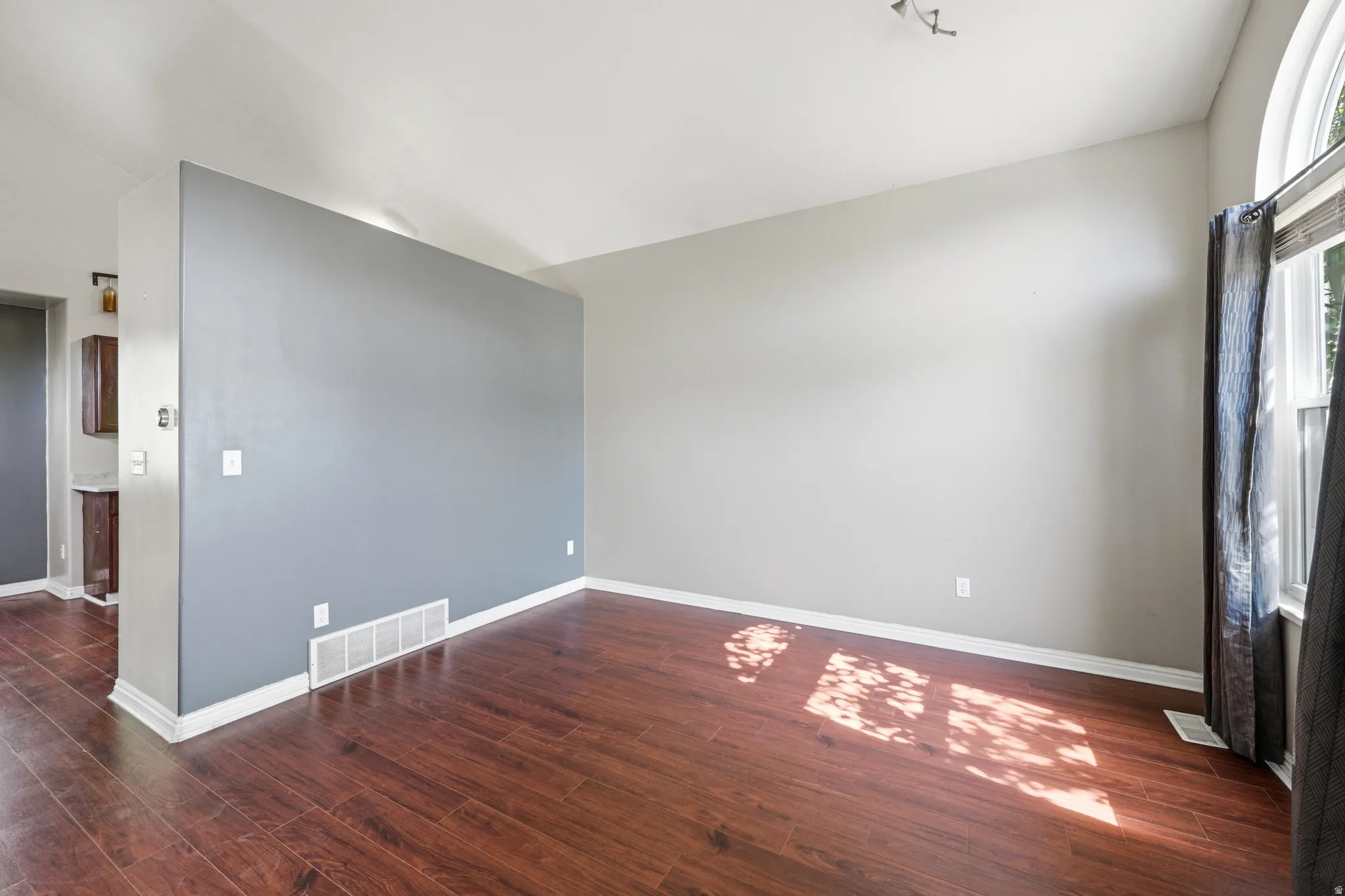 Spacious room featuring wood-finish flooring, a contemporary semi-flush mount ceiling light, and an arched window with roller shades
