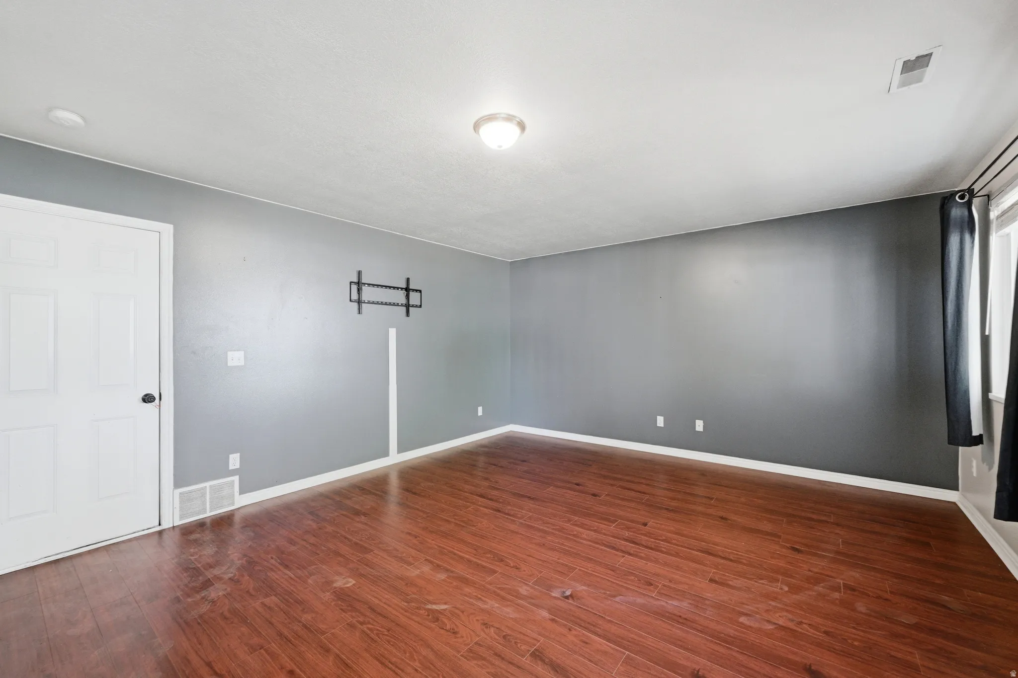 Spacious interior room featuring wood-finish flooring, light gray wall paint, and white trim