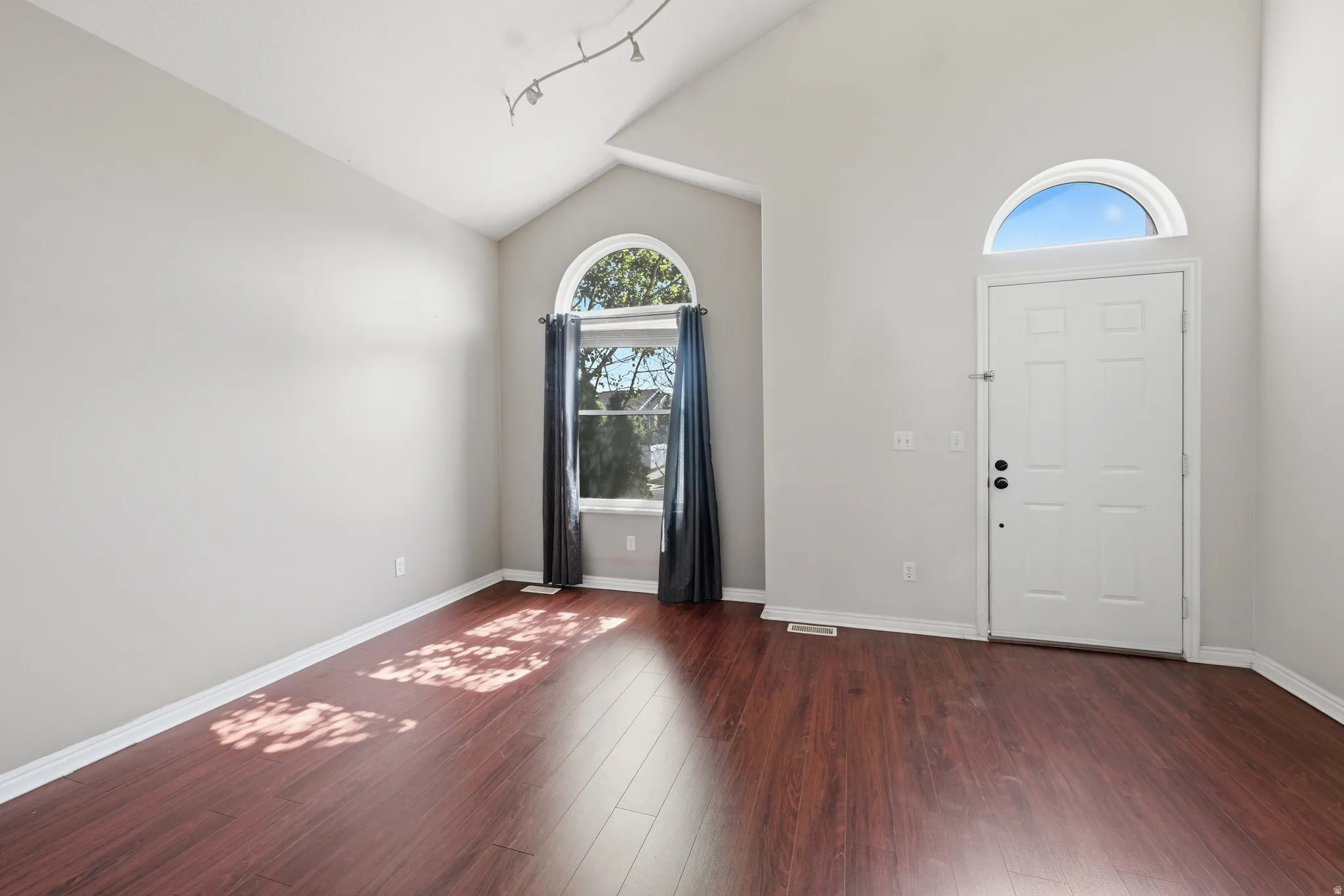 Spacious entry area featuring vaulted ceilings, rich wood-finish flooring, and a white front door with an arched transom window