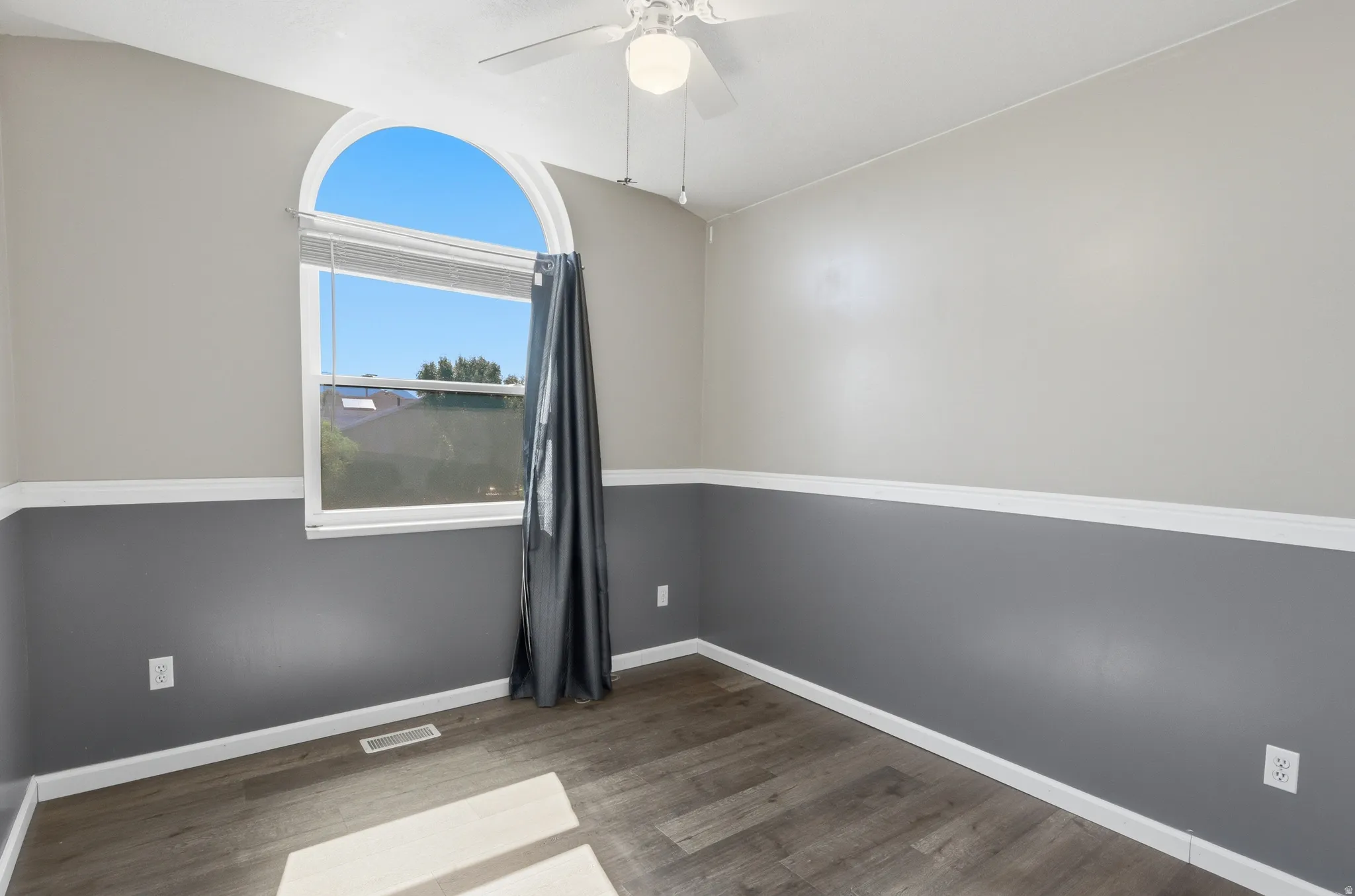 Room featuring an arched window, wood-finish flooring, two-tone wall treatment, and a ceiling fan