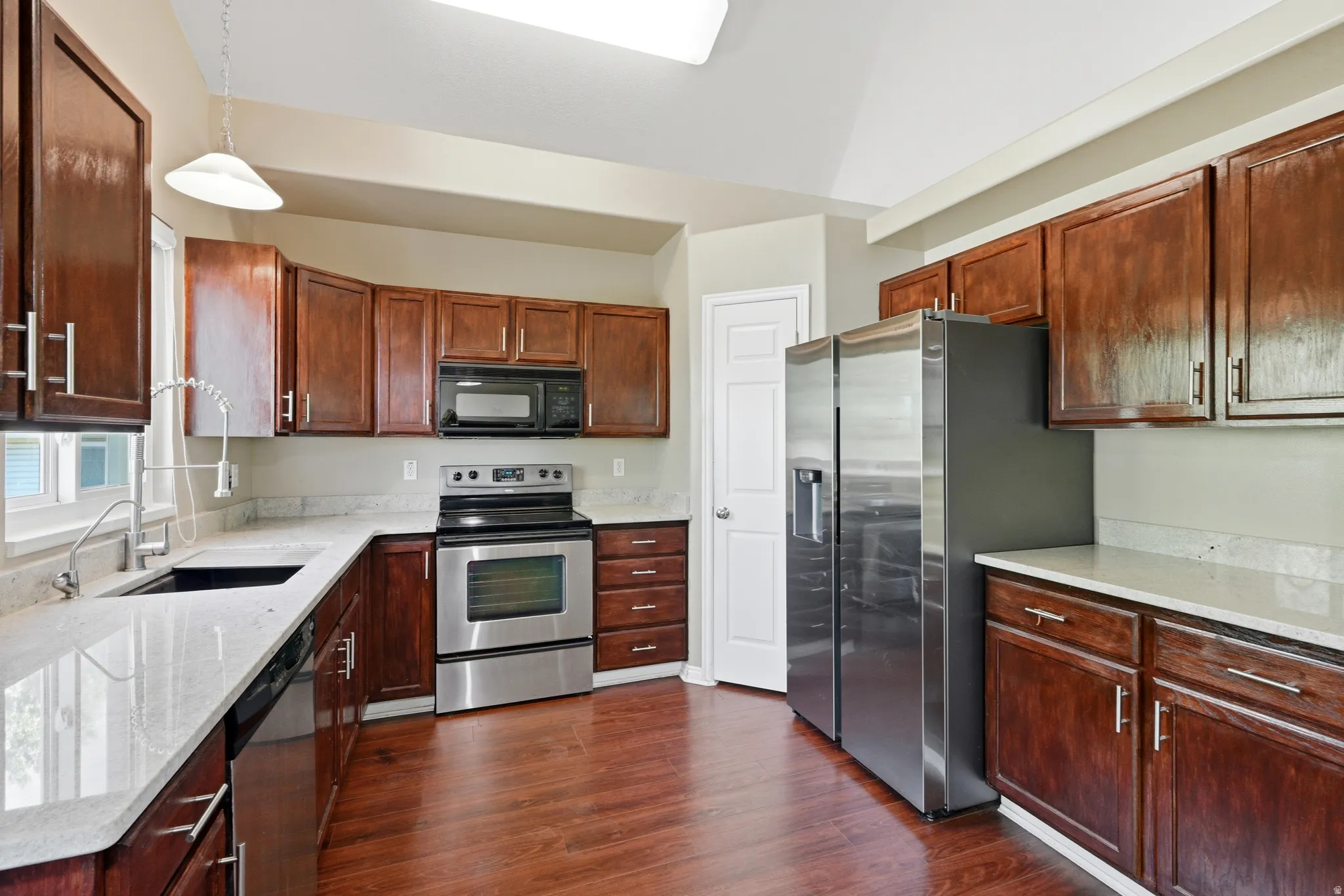 Kitchen featuring wood-finish flooring, stainless steel appliances, light-toned countertops, dark wood cabinetry, and a vaulted ceiling