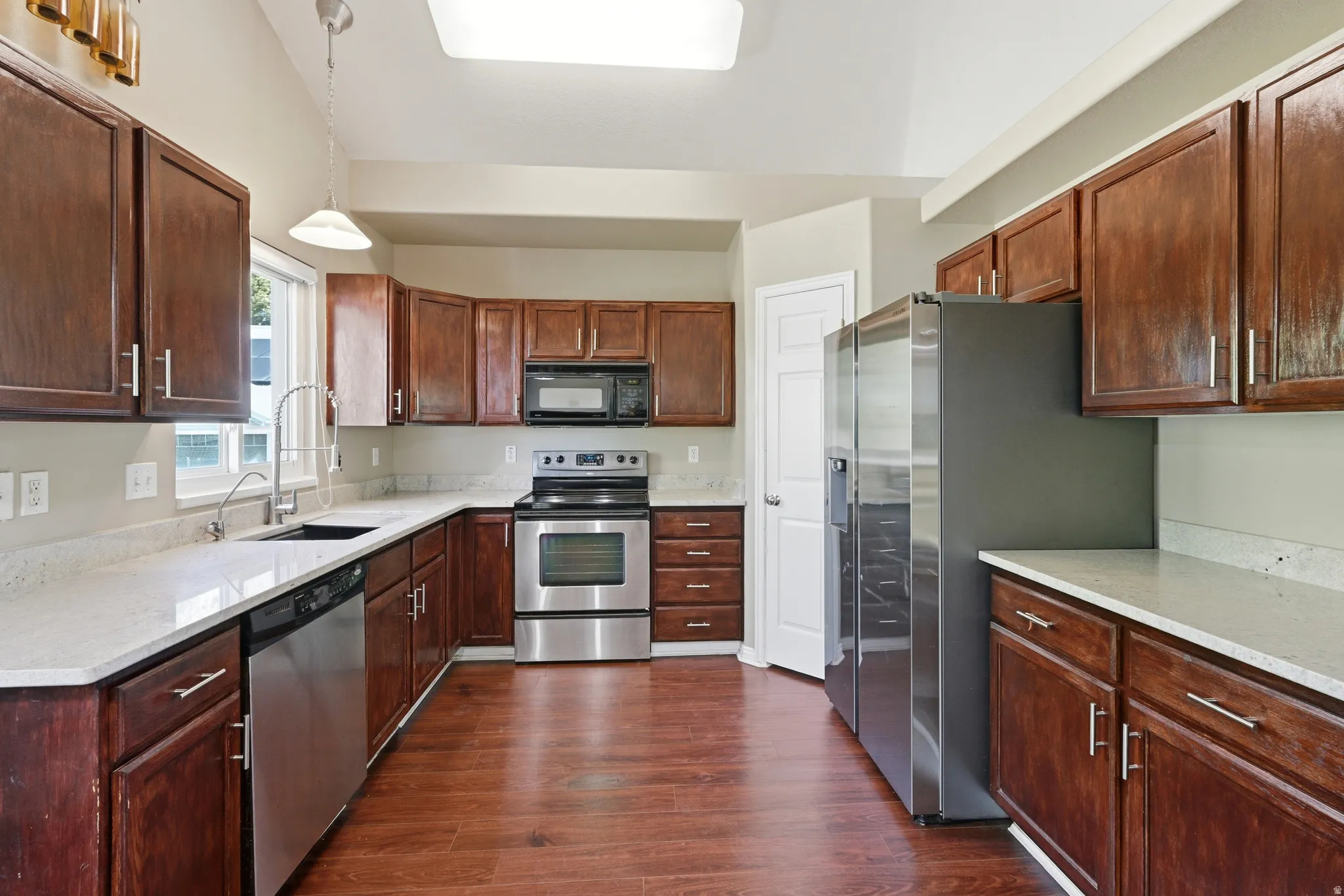 Kitchen featuring wood-finish flooring, dark wood cabinetry, light-toned countertops, and stainless steel appliances