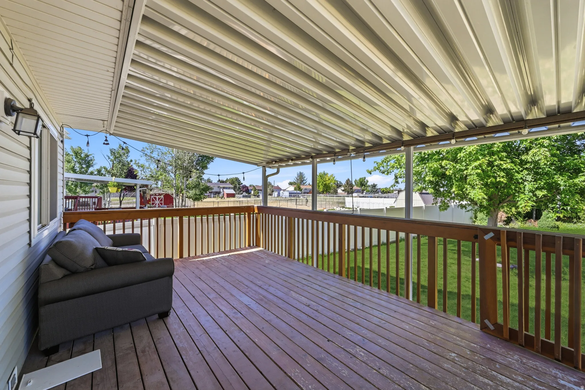 Expansive covered deck featuring wood-finish decking, a sturdy wooden railing, and a corrugated metal patio cover
