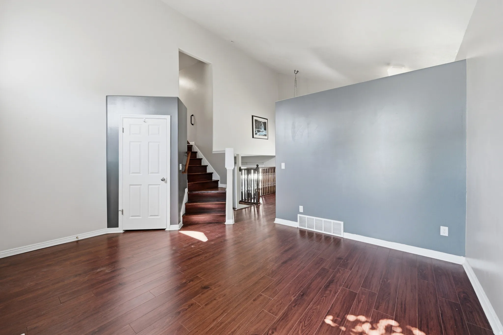 Spacious interior with vaulted ceilings, wood-finish flooring, a contemporary accent wall, and a prominent staircase with wood treads