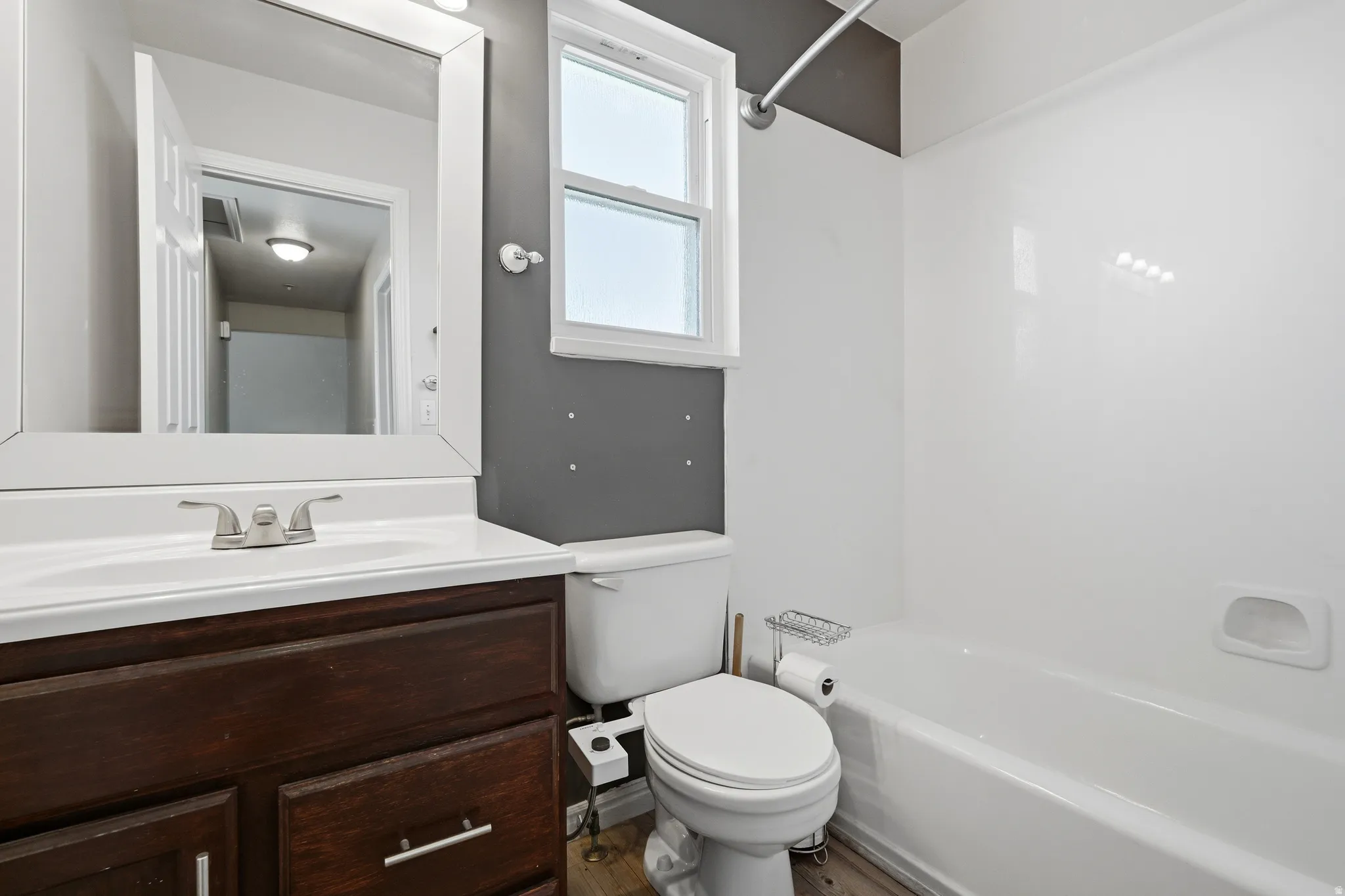 Bathroom featuring a white bathtub, toilet, and wood-finish vanity with an integrated sink