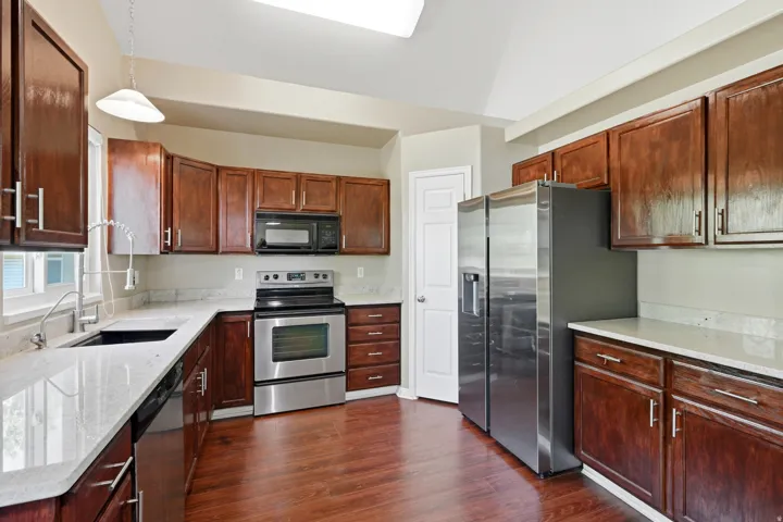 Kitchen featuring wood-finish flooring, stainless steel appliances, light-toned countertops, dark wood cabinetry, and a vaulted ceiling