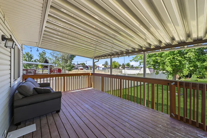 Expansive covered deck featuring wood-finish decking, a sturdy wooden railing, and a corrugated metal patio cover
