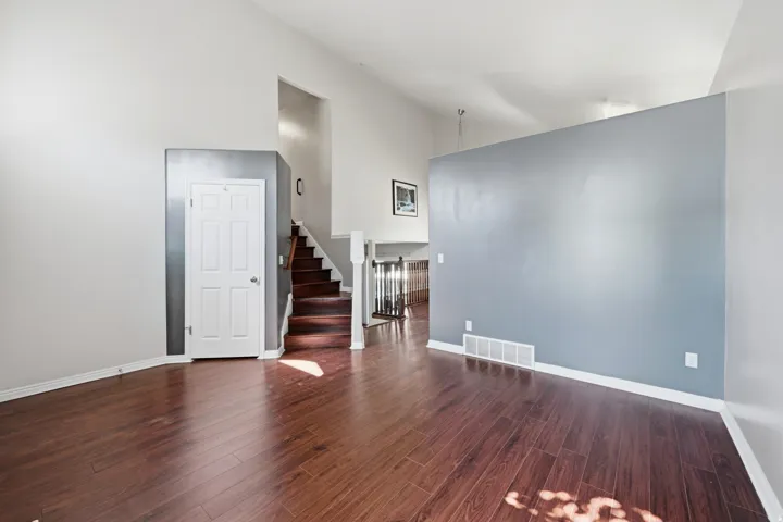 Spacious interior with vaulted ceilings, wood-finish flooring, a contemporary accent wall, and a prominent staircase with wood treads
