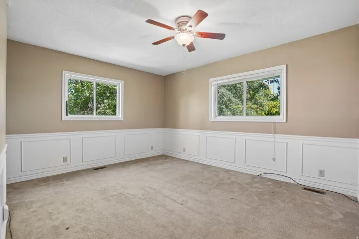 Spacious room featuring neutral carpeting, chair rail molding, and two windows offering exterior views