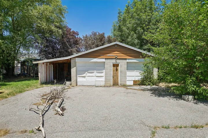 Structure featuring a two-car garage with white doors, a central wooden entry door, and a brown siding gable