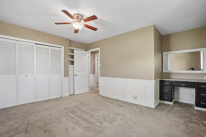 Neutral-toned room featuring a wood-finish ceiling fan with integrated lighting, extensive wainscoting, and carpet flooring