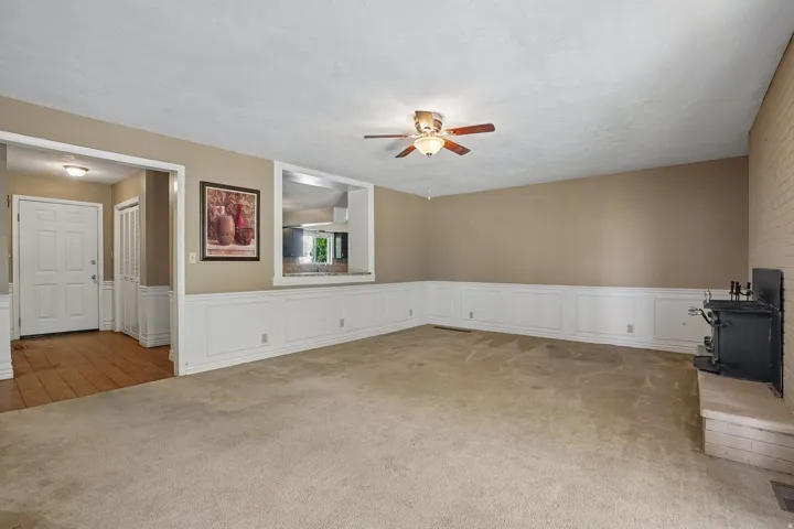 Carpeted living area featuring wainscoting, a ceiling fan with light fixture, and a brick fireplace with a hearth