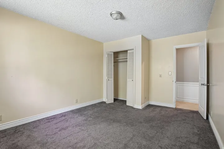 Carpeted room featuring a ceiling-mounted light fixture, bi-fold closet doors, and light-toned wall paint with white baseboards