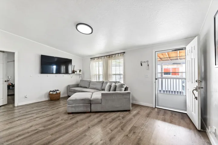 Spacious living area featuring wood-finish flooring, white walls, and a contemporary flush-mount ceiling light