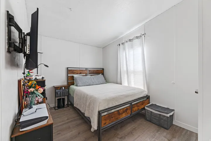 Bedroom featuring wood-finish flooring, white paneling, and a window with white blinds