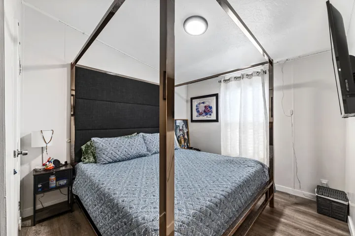 Bedroom featuring wood-finish flooring, a wall-mounted television, white walls, and a flush-mount ceiling light fixture