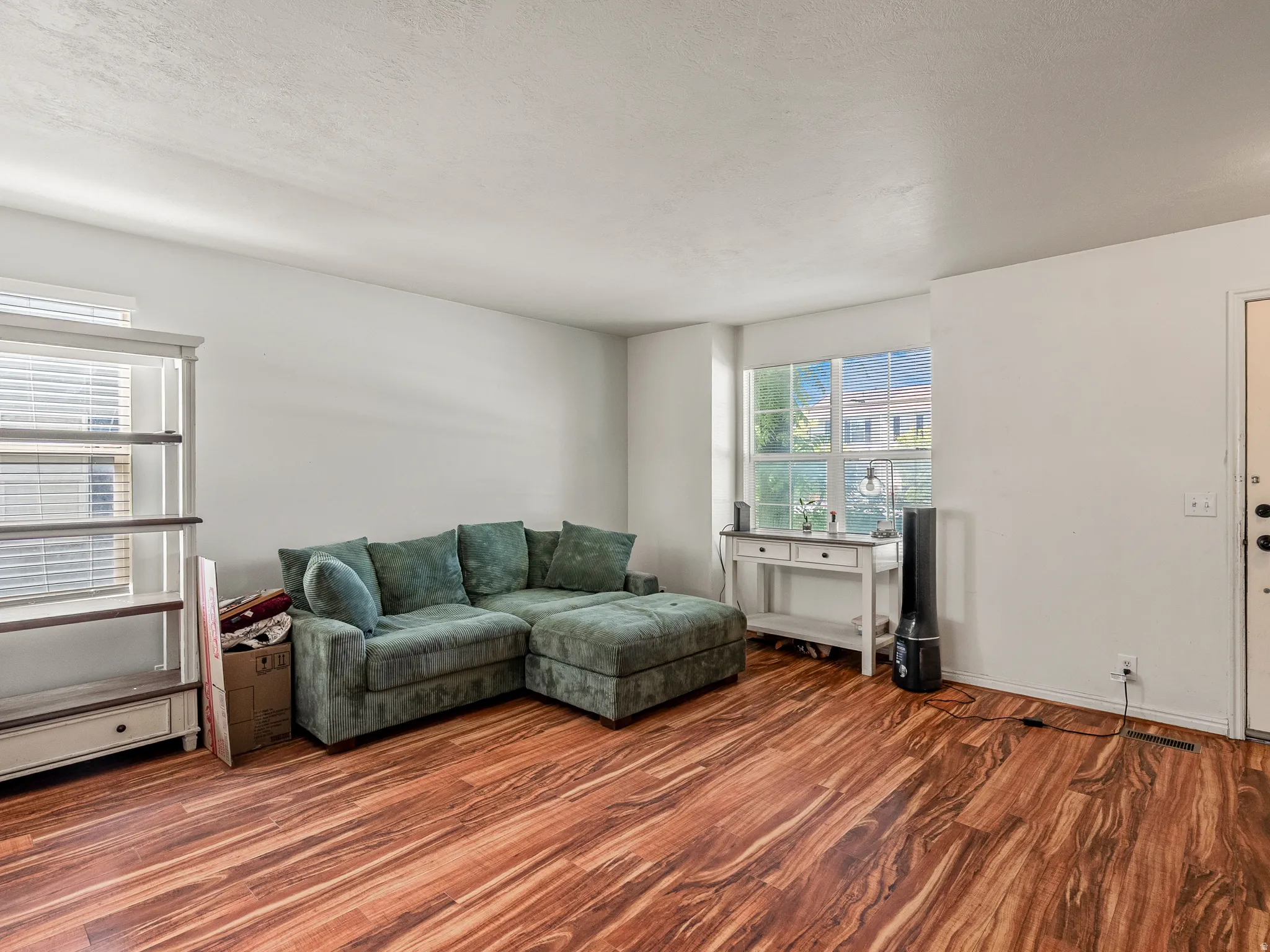 Spacious living area featuring wide plank wood-finish flooring, white wall tones, and ample natural light from a large window
