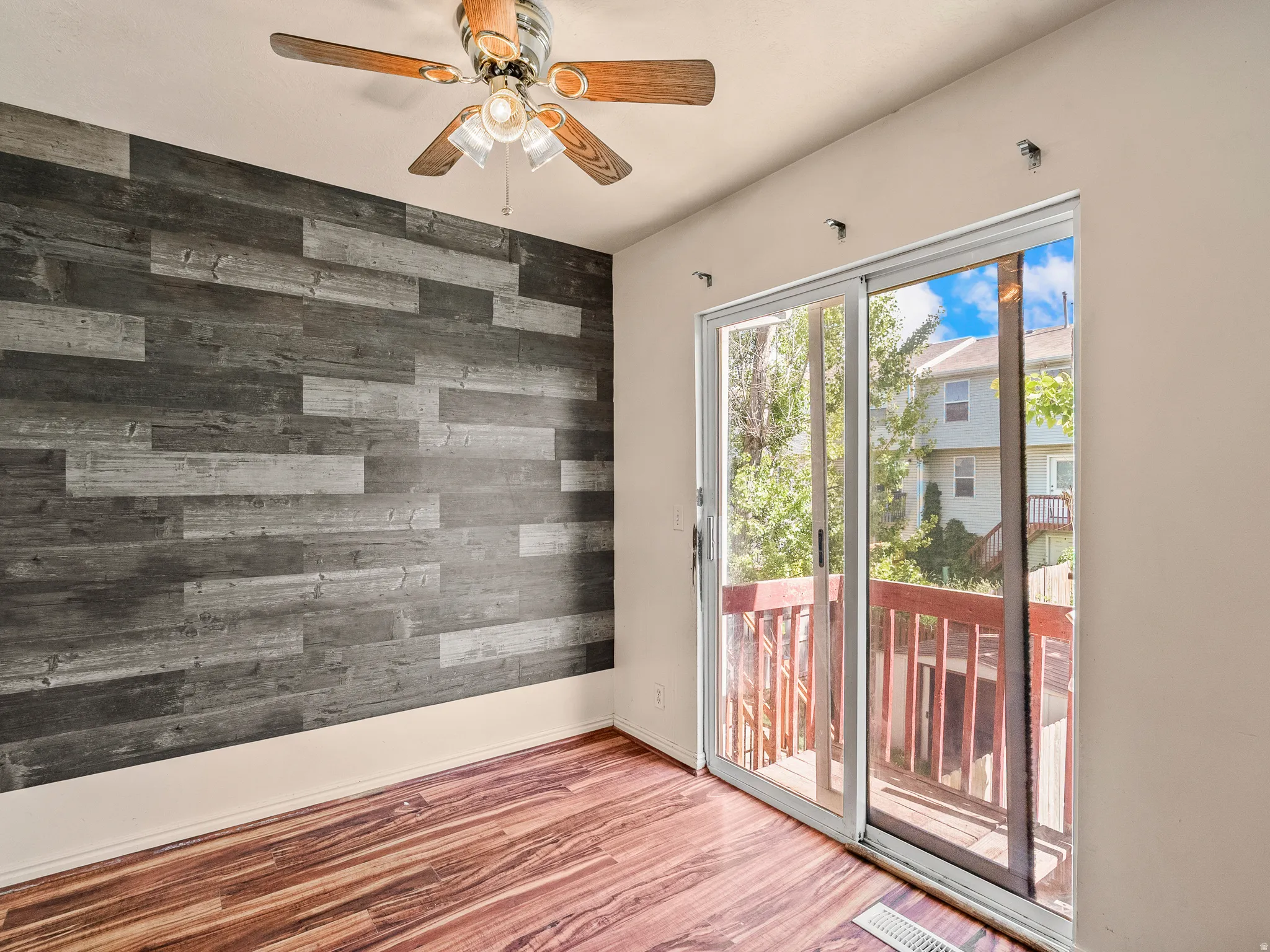 Accent wall with horizontal wood-finish planks, wood-finish flooring, and a ceiling fan with integrated lighting