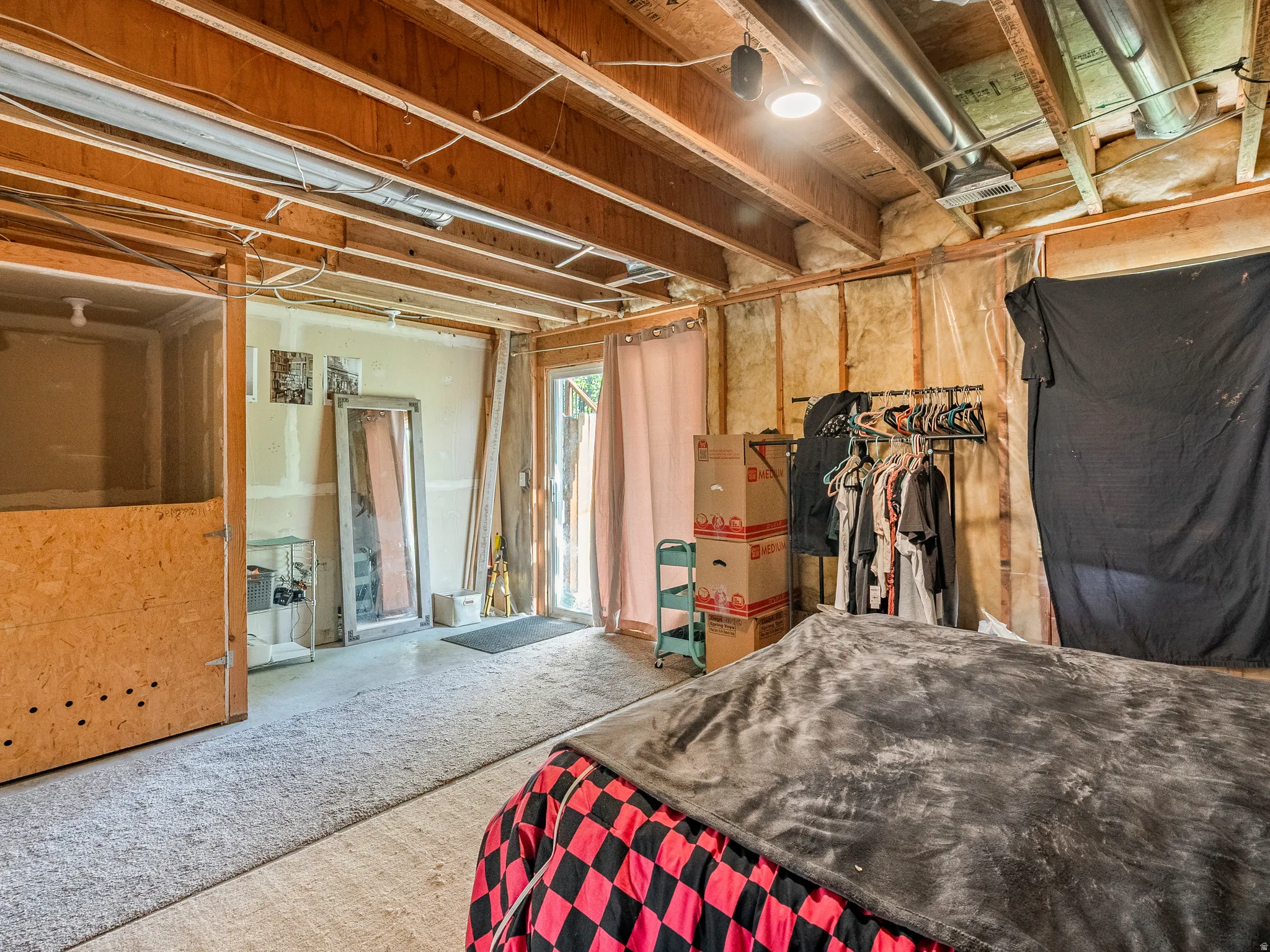 Unfinished basement space featuring exposed wood joists and subflooring, a carpeted area, and a visible exterior door