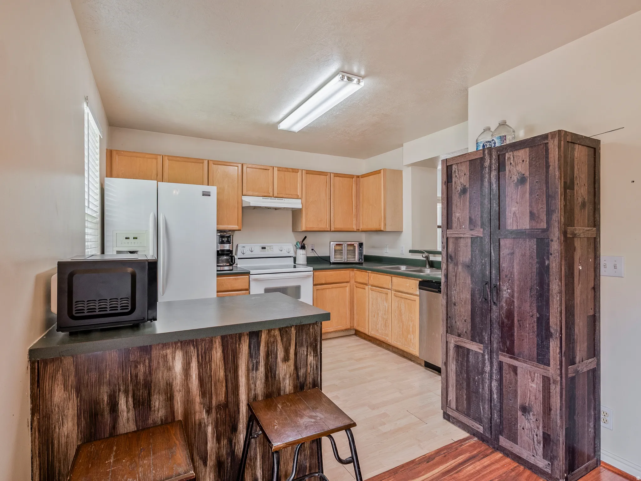 Kitchen featuring light wood-finish cabinetry, white appliances, and light wood-finish flooring