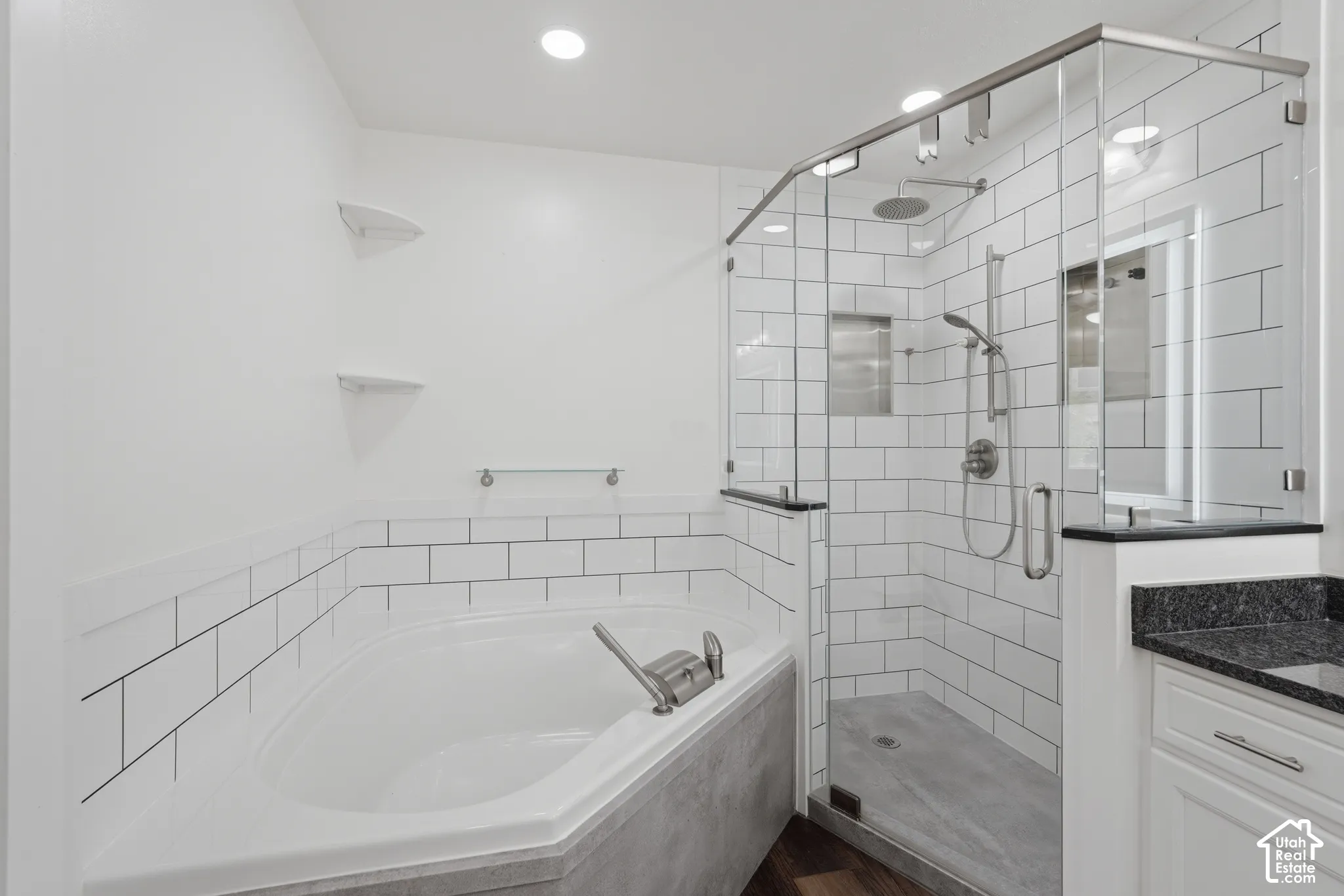 Contemporary bathroom featuring a corner soaking tub, a frameless glass shower with subway tile surround, a built-in shower niche, and a vanity with a dark countertop