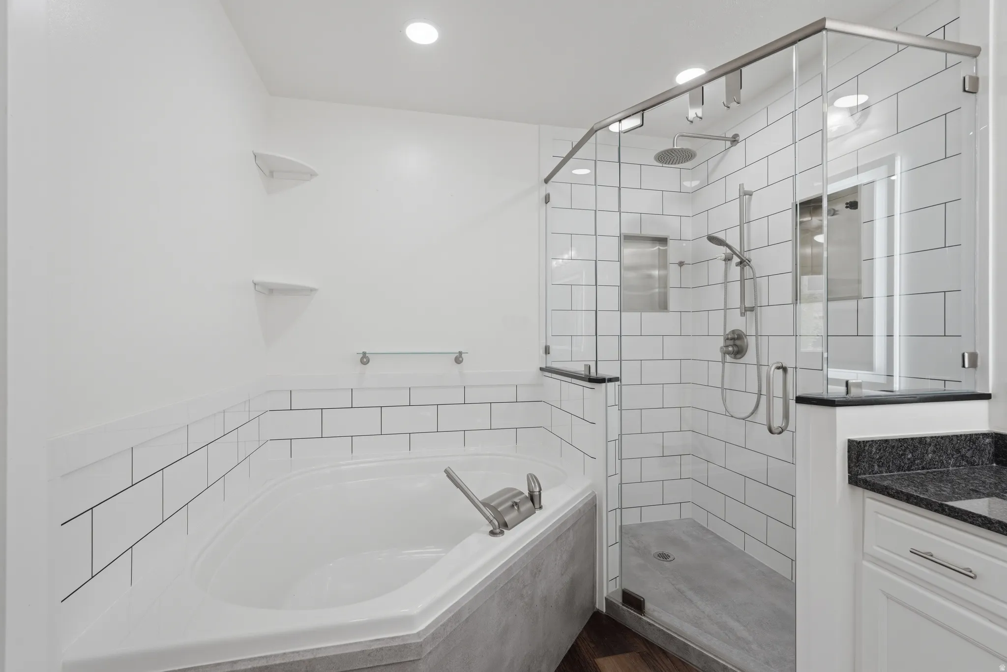 Contemporary bathroom featuring a corner soaking tub, a frameless glass shower with subway tile surround, a built-in shower niche, and a vanity with a dark countertop