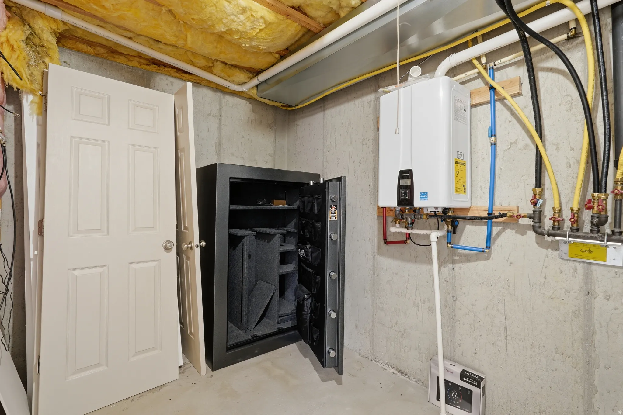 Utility area featuring a tankless water heater, exposed concrete foundation walls, and visible ceiling insulation