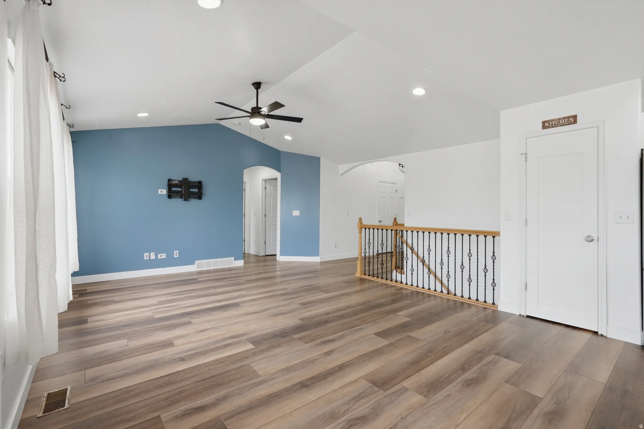 Spacious living area featuring wood-finish flooring, a vaulted ceiling, recessed lighting, and a modern ceiling fan